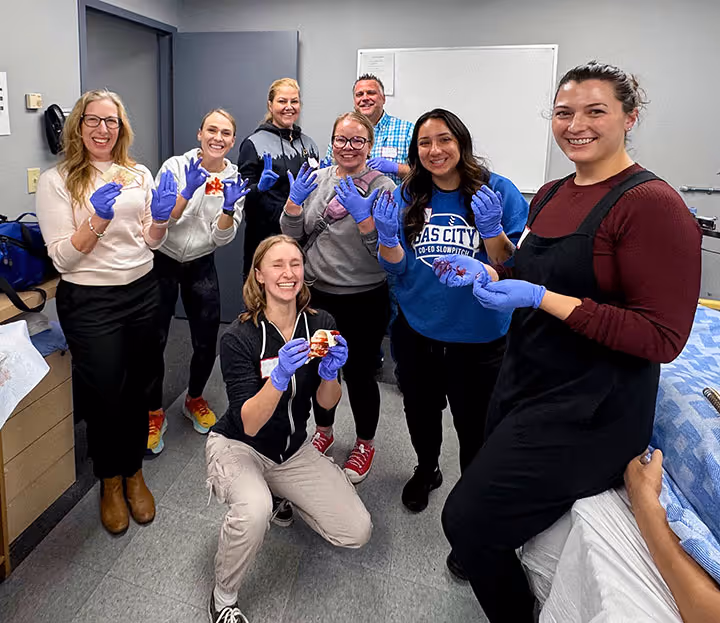 Group of people in gloves holding anatomical heart models and smiling in a lab classroom.