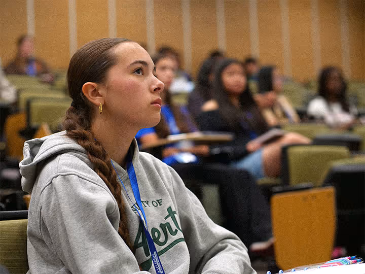 Young woman with braided hair attentively listening in a lecture hall with other students.