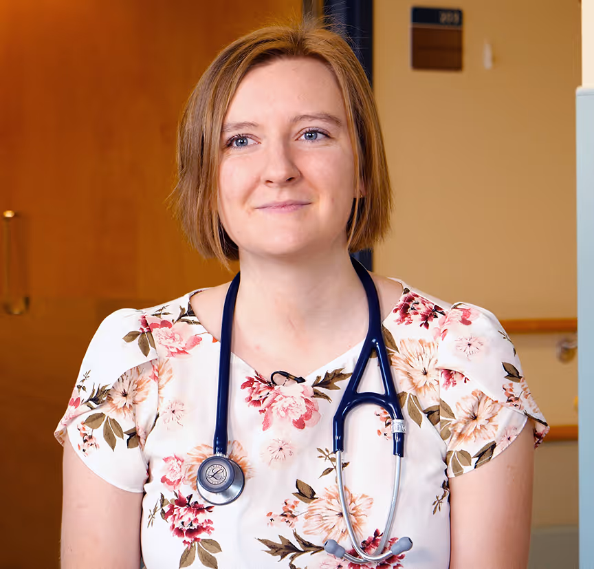 Young female doctor wearing floral top with stethoscope around her neck smiling indoors.