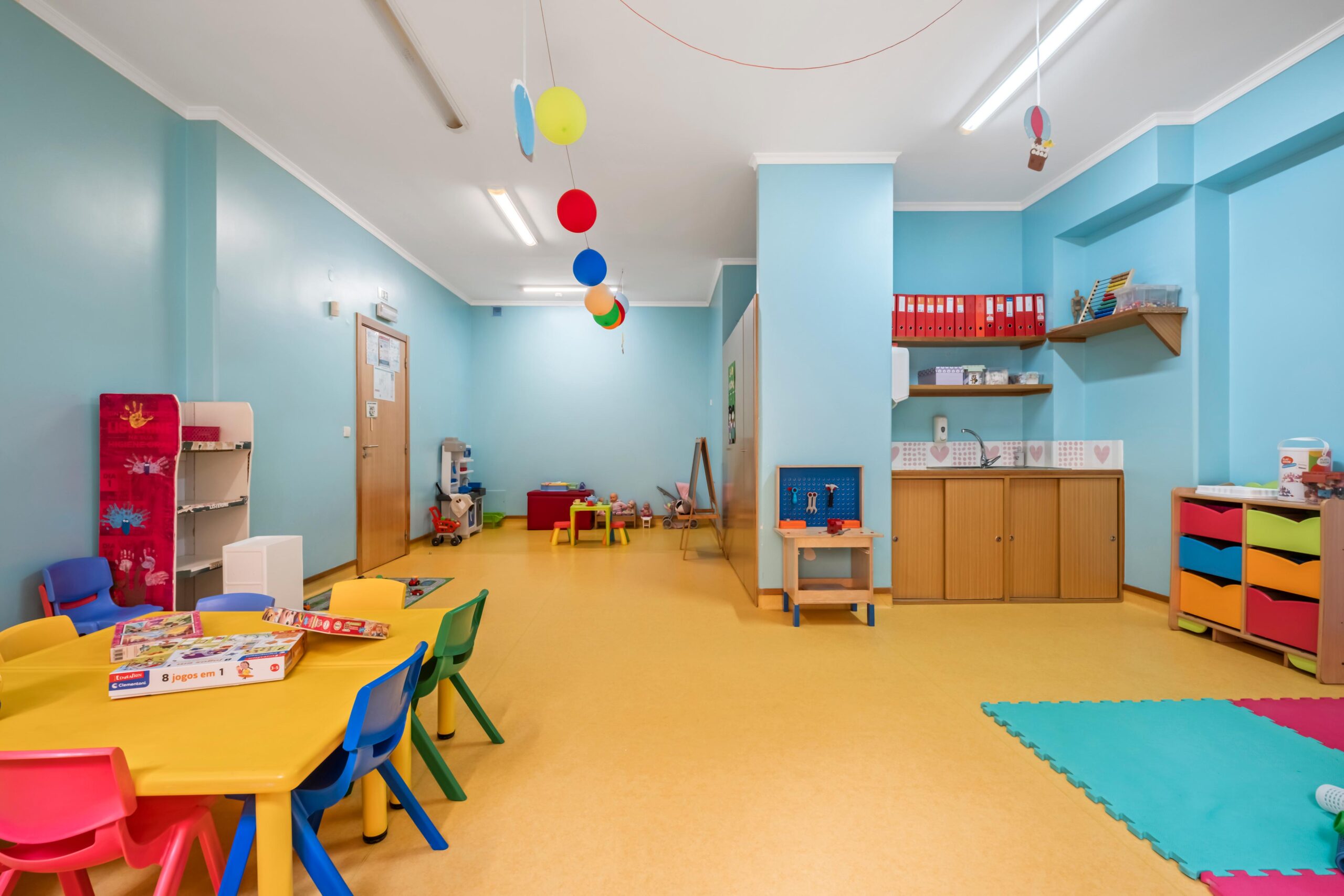 Sala jardim de infância Texugos com mesas, cadeiras, tapete e diversos brinquedos, no infantário A Toca dos Traquinas