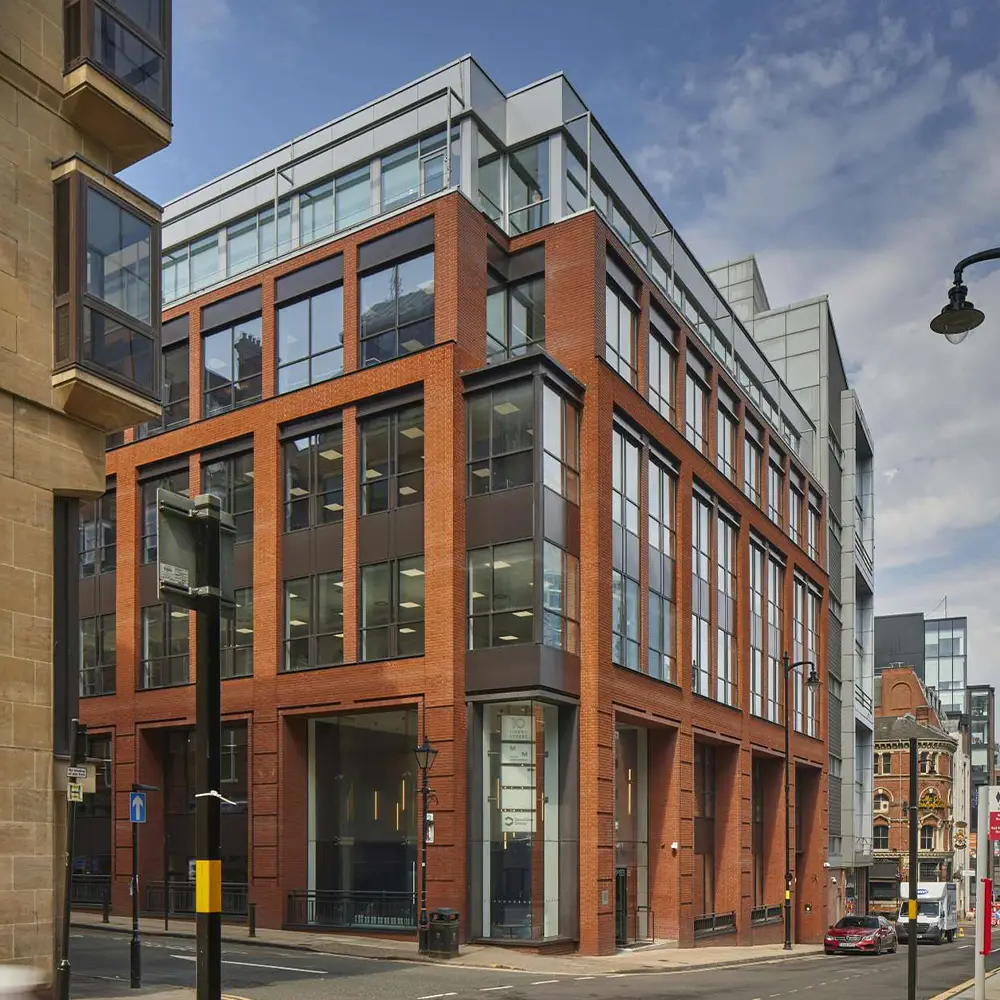 Modern brick and glass office building on a city street corner under a partly cloudy sky.