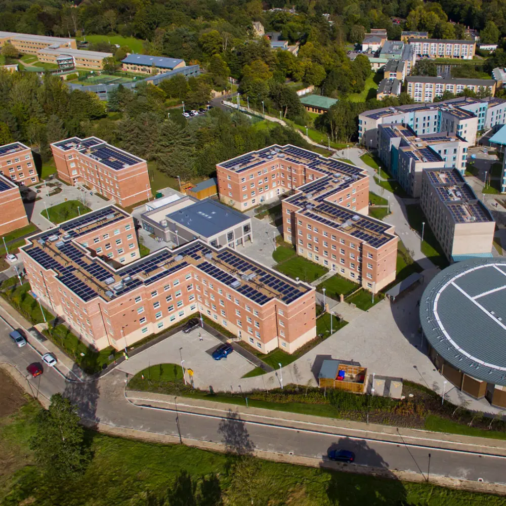 Aerial view of a campus with multiple brick buildings topped with solar panels surrounded by greenery.