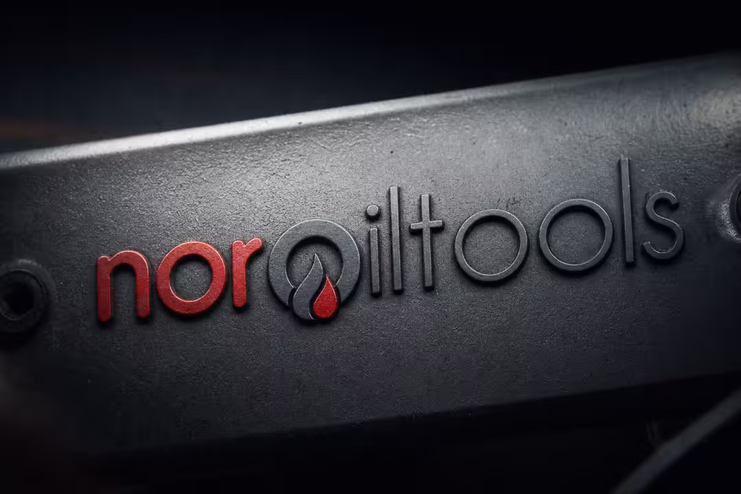 An extreme close-up of the noroiltools brand logo sharply embossed onto a dark, textured cast-iron piece of oilfield equipment.