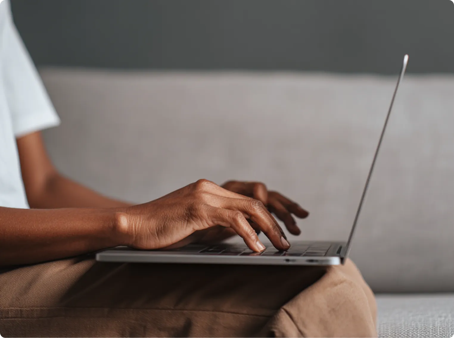 Close-up of a person typing on a laptop keyboard while sitting on a couch.