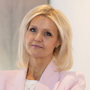 Portrait of a middle-aged woman with blonde hair wearing a light pink blazer.
