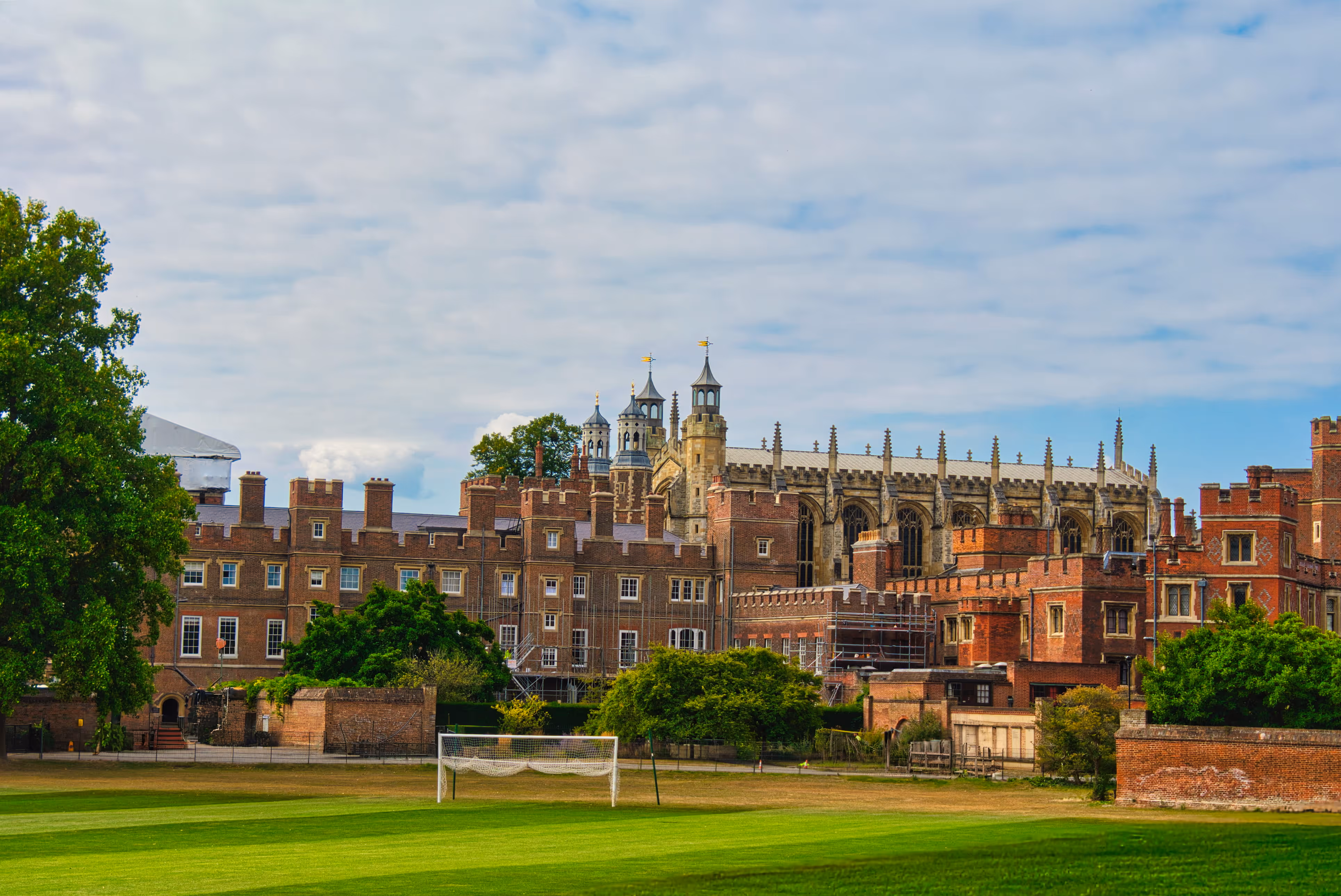 Historic brick castle with towers and a church behind a green soccer field with a goal net.