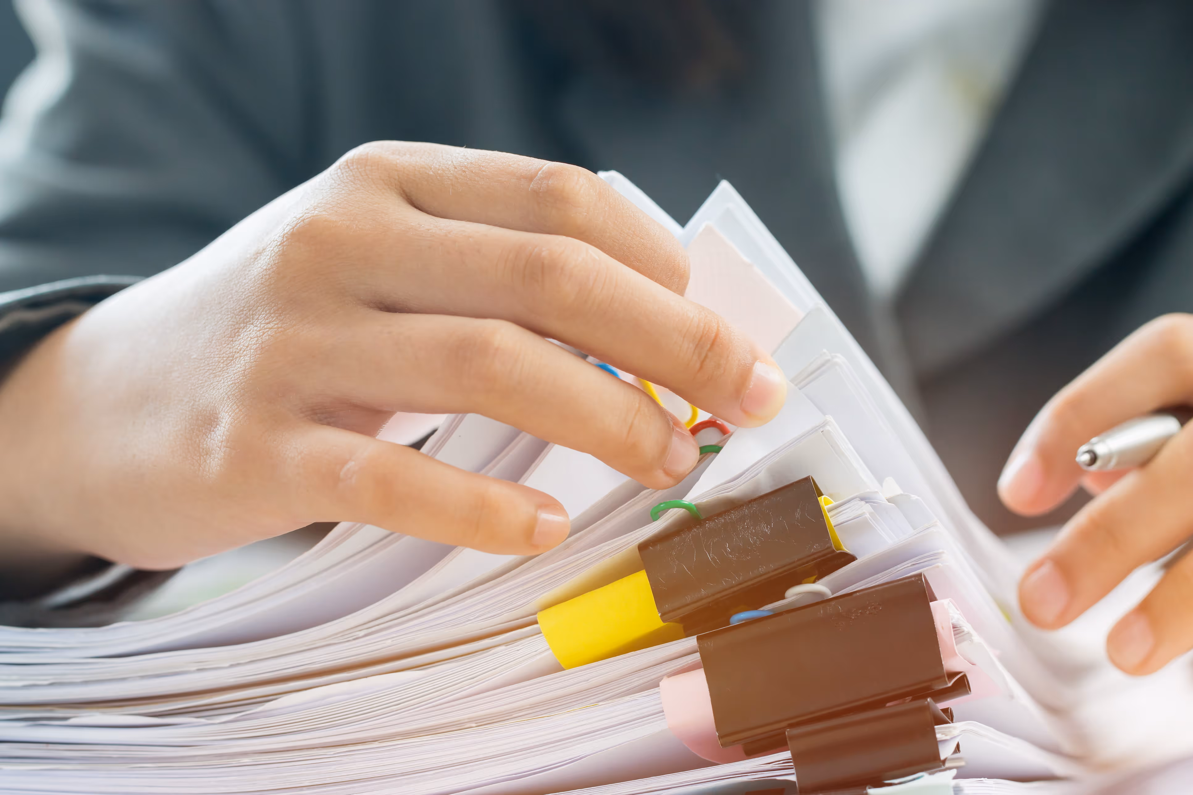 Close-up of hands organizing thick stack of document papers with binder clips and colored tabs.
