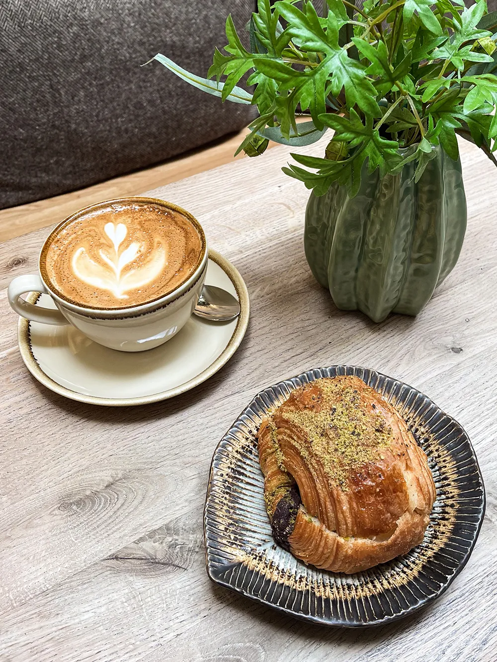 A rustic scone with berries sits on a dark plate next to a small black pot of cream. A silver spoon adds elegance, evoking a cozy and inviting atmosphere.