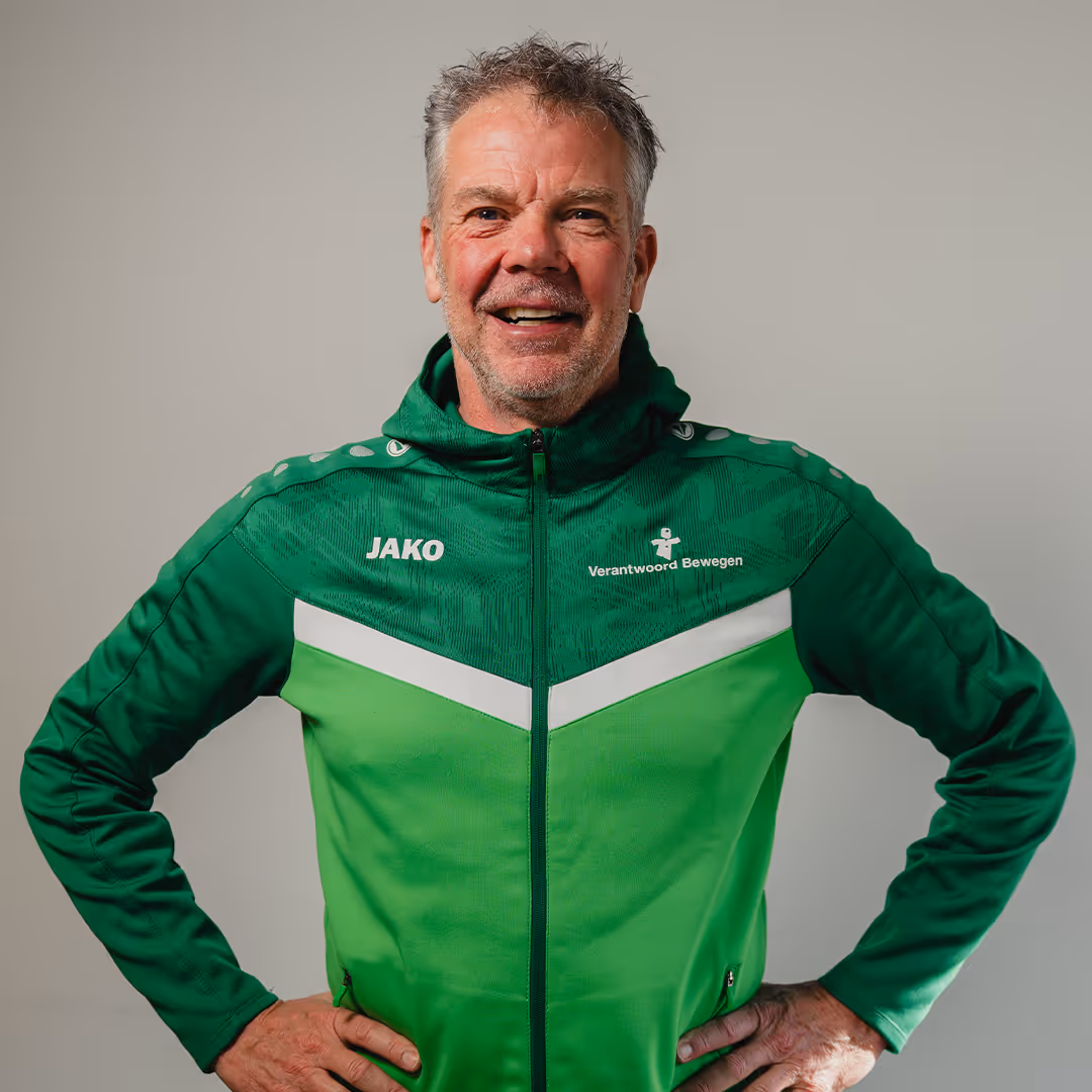 Middle-aged man smiling with hands on hips wearing a green and dark green JAKO zip-up sports jacket.
