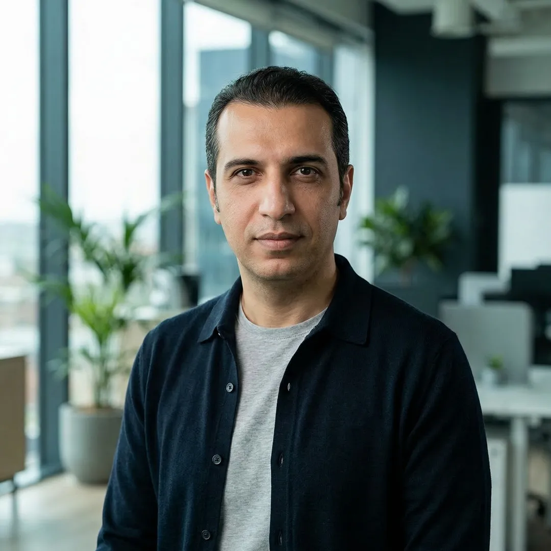 Man with short dark hair wearing a dark jacket and gray shirt in a modern office with plants.
