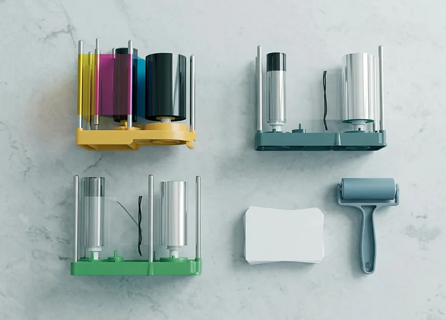 Three colored label printer cartridges, a stack of white labels, and a blue adhesive roller on a gray surface.