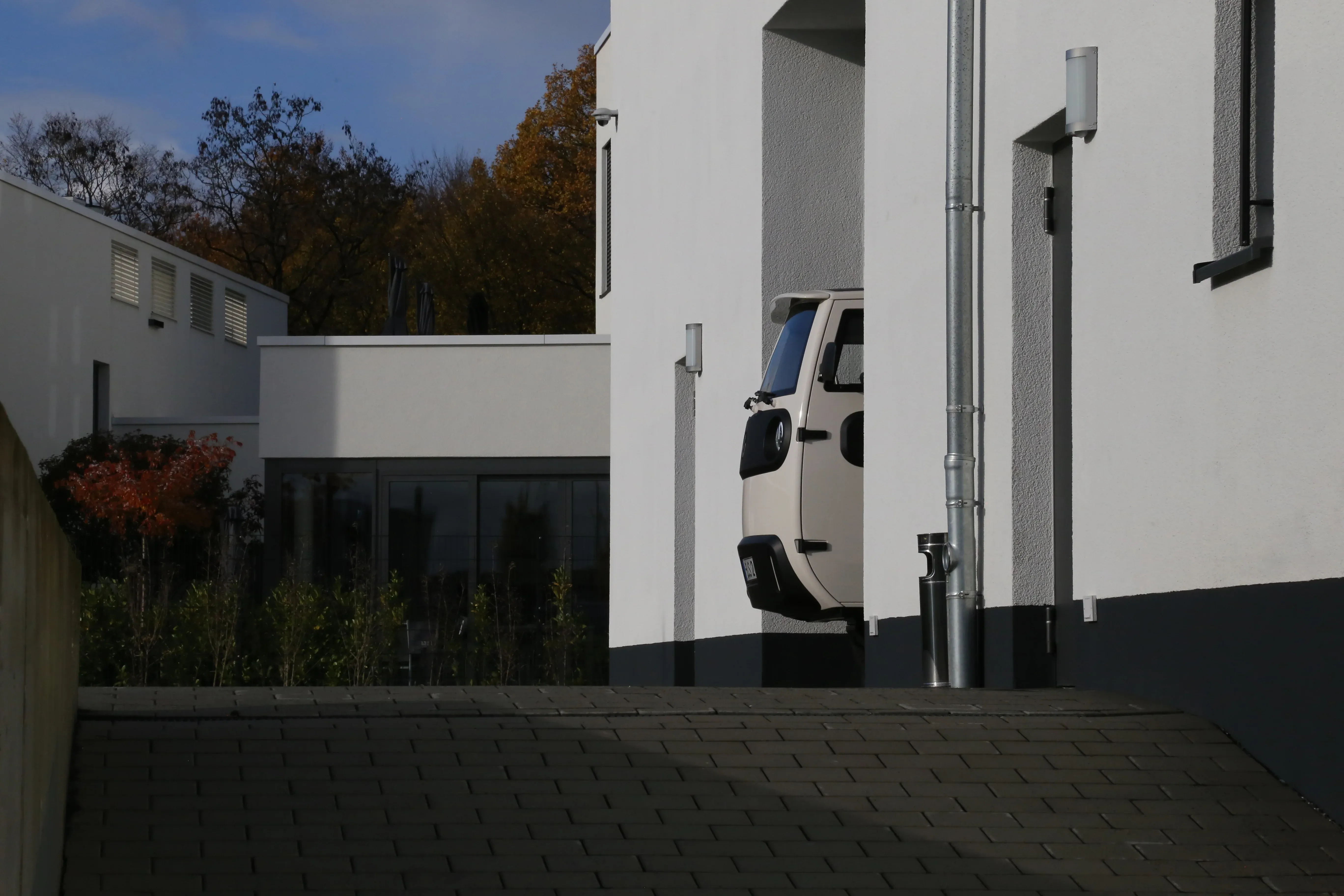 Side view of a small beige car partially parked in a modern white building's garage.