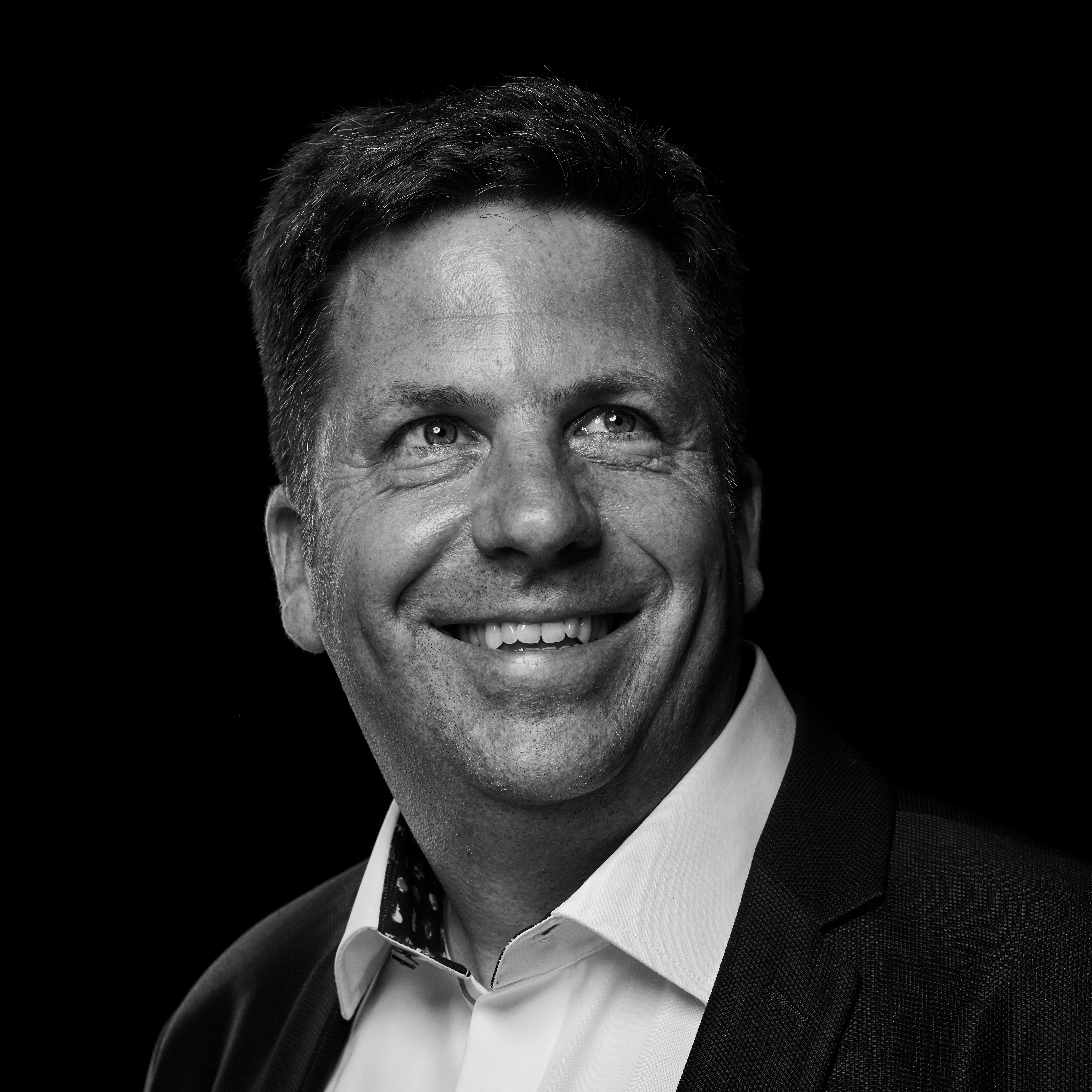 Lächelnder Mann in Anzug mit weißem Hemd vor schwarzem Hintergrund.