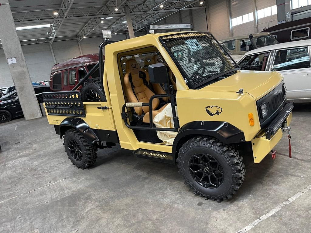 Small yellow off-road utility truck with large knobby tires and tan bucket seats parked indoors.