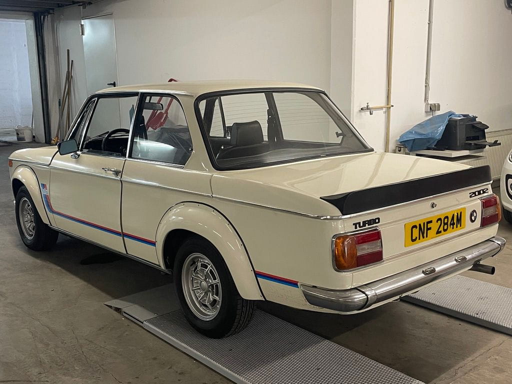 White classic AMC car with Turbo badge and black rear spoiler parked inside a garage.