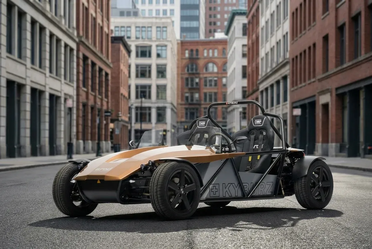 Open-frame two-seater sports car with gold and black body parked on an urban street with brick buildings.