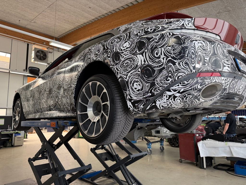 Car with black and white swirl camouflage pattern raised on hydraulic lifts inside a workshop.