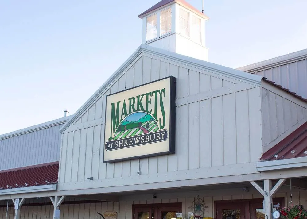 White wooden building with a sign reading 'Markets at Shrewsbury' featuring a landscape illustration.