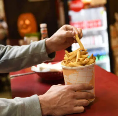 Person picking a french fry from a large cup filled with fries on a red counter.