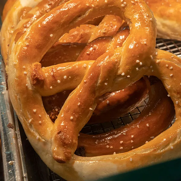 Close-up of freshly baked soft pretzels sprinkled with coarse salt on a cooling rack.