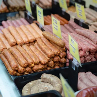 Display of various types of sausages arranged in trays with yellow price tags in a market.