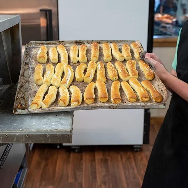 Person holding a large baking tray filled with freshly baked soft pretzel rods sprinkled with coarse salt.