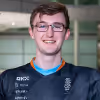 Lucas Blakeley - Smiling young man wearing glasses and a dark sports jersey standing indoors.