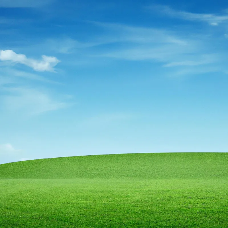 Rolling green grassy hill under a blue sky with scattered white clouds.