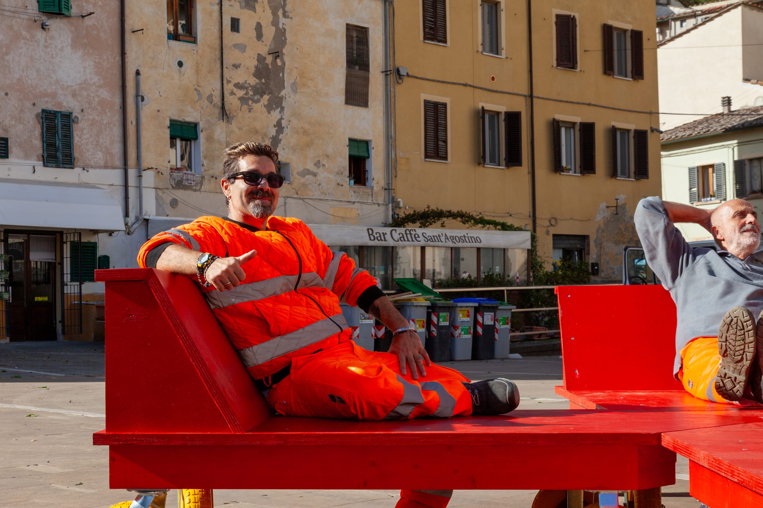 Due persone in abiti da lavoro si rilassano su sedute rosse in una piazza
