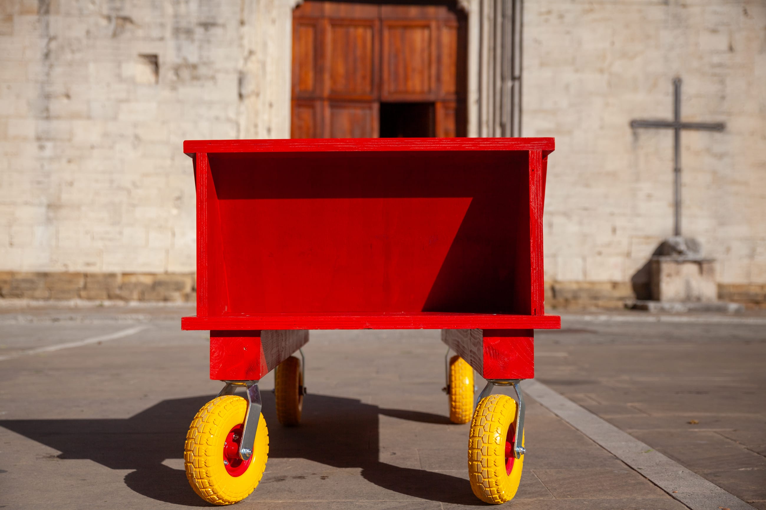 Modulo rosso su ruote gialle visto di fronte, davanti alla facciata in pietra di una chiesa