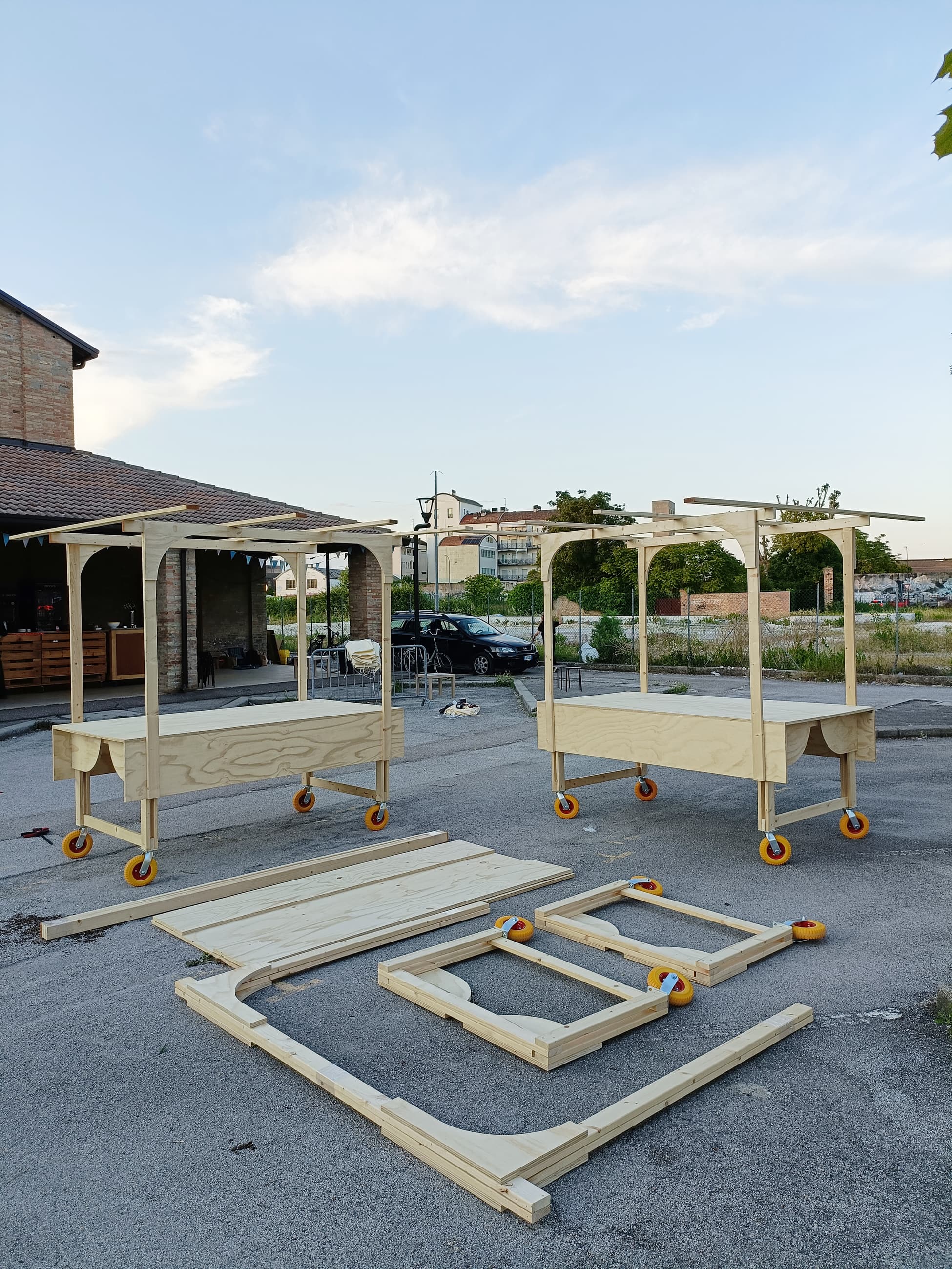 Due padiglioni in legno su ruote e altri elementi da montare a terra, in un piazzale