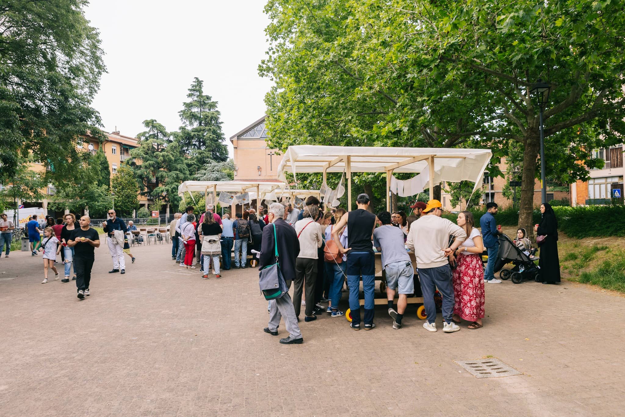 Folla attorno ai padiglioni in legno su ruote, in un viale tra gli alberi