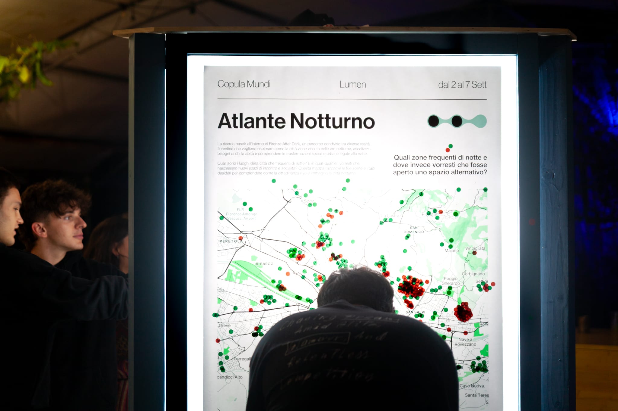 Persone di sera davanti a un pannello luminoso con una mappa segnata da punti colorati