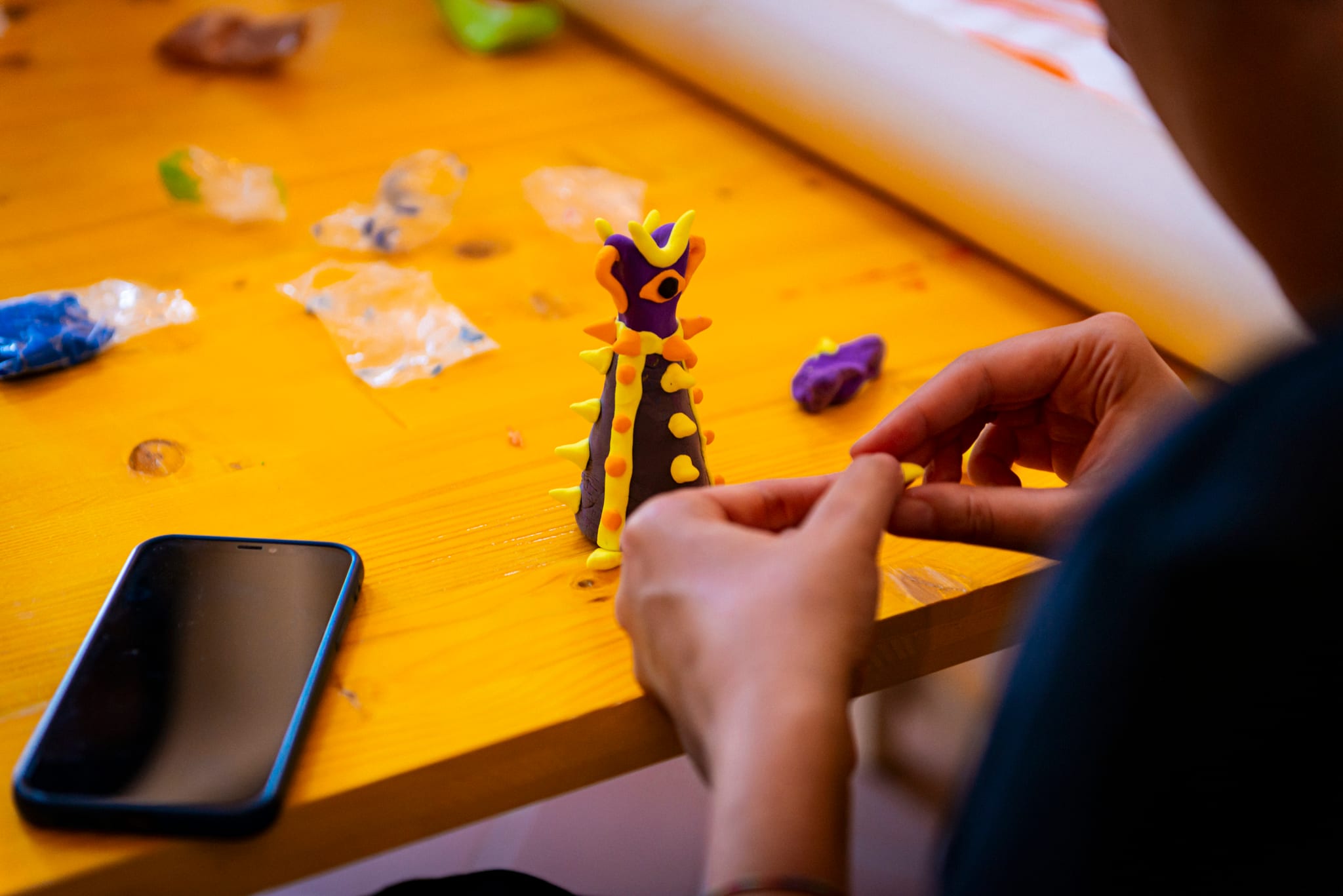 Mani modellano una figura in plastilina colorata su un tavolo in legno giallo