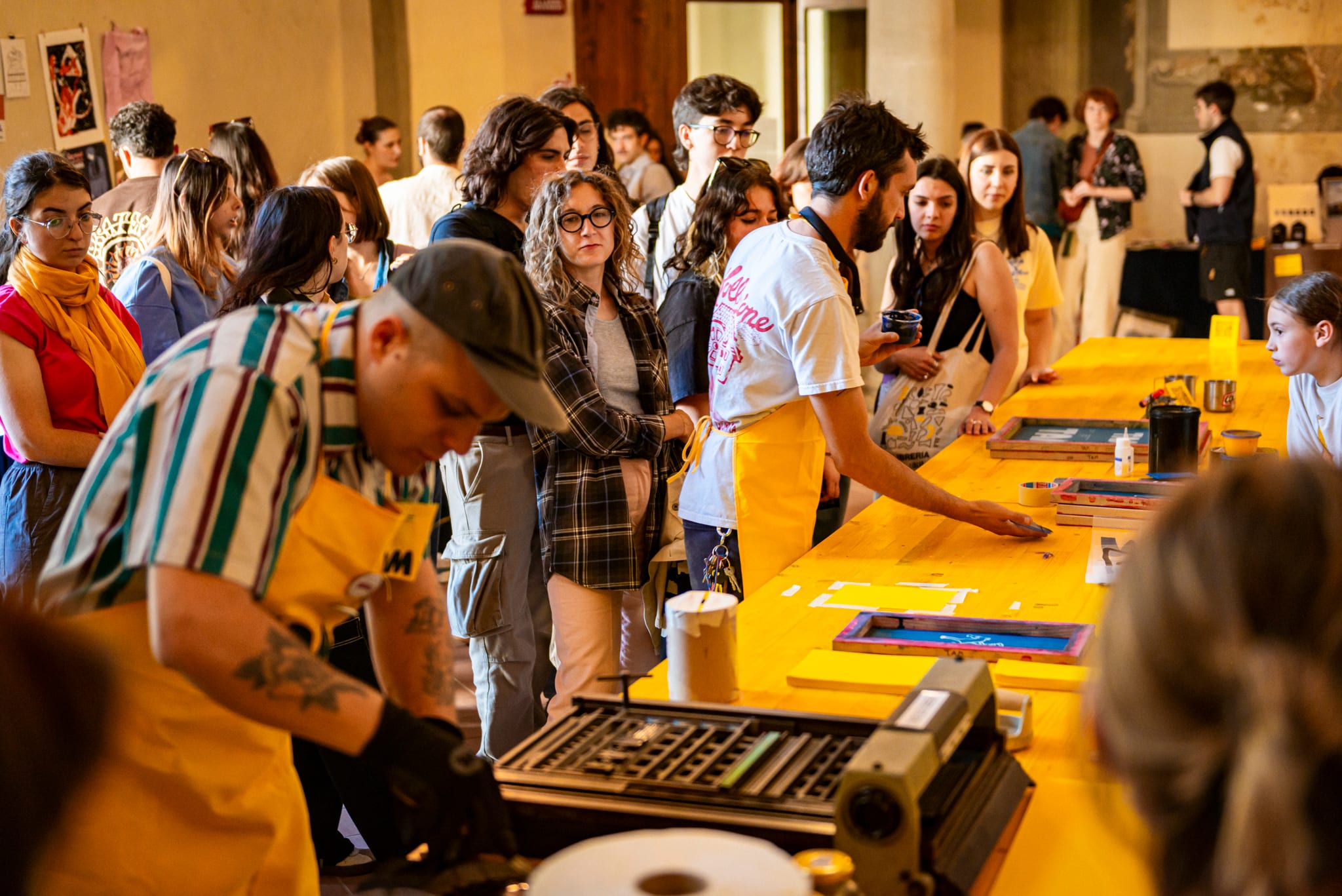 Persone attorno a un lungo tavolo giallo mentre una persona stampa in serigrafia