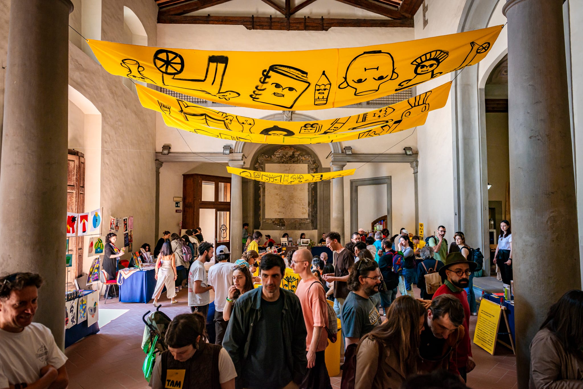 Salone storico affollato, con grandi teli gialli illustrati appesi al soffitto