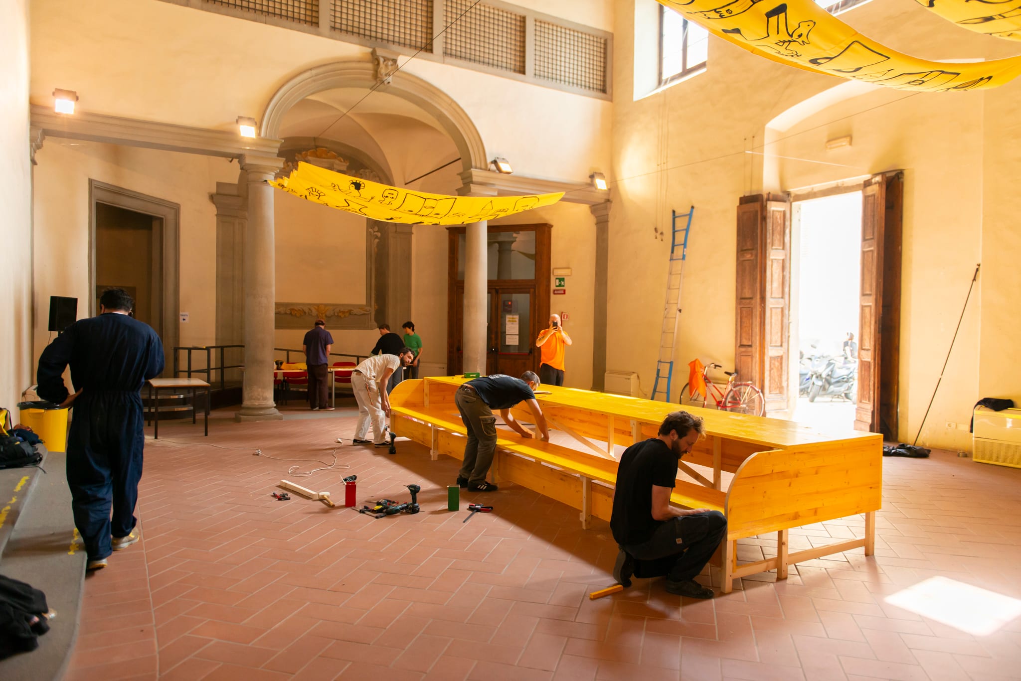 Persone montano lunghe panche in legno giallo in un salone storico ancora vuoto