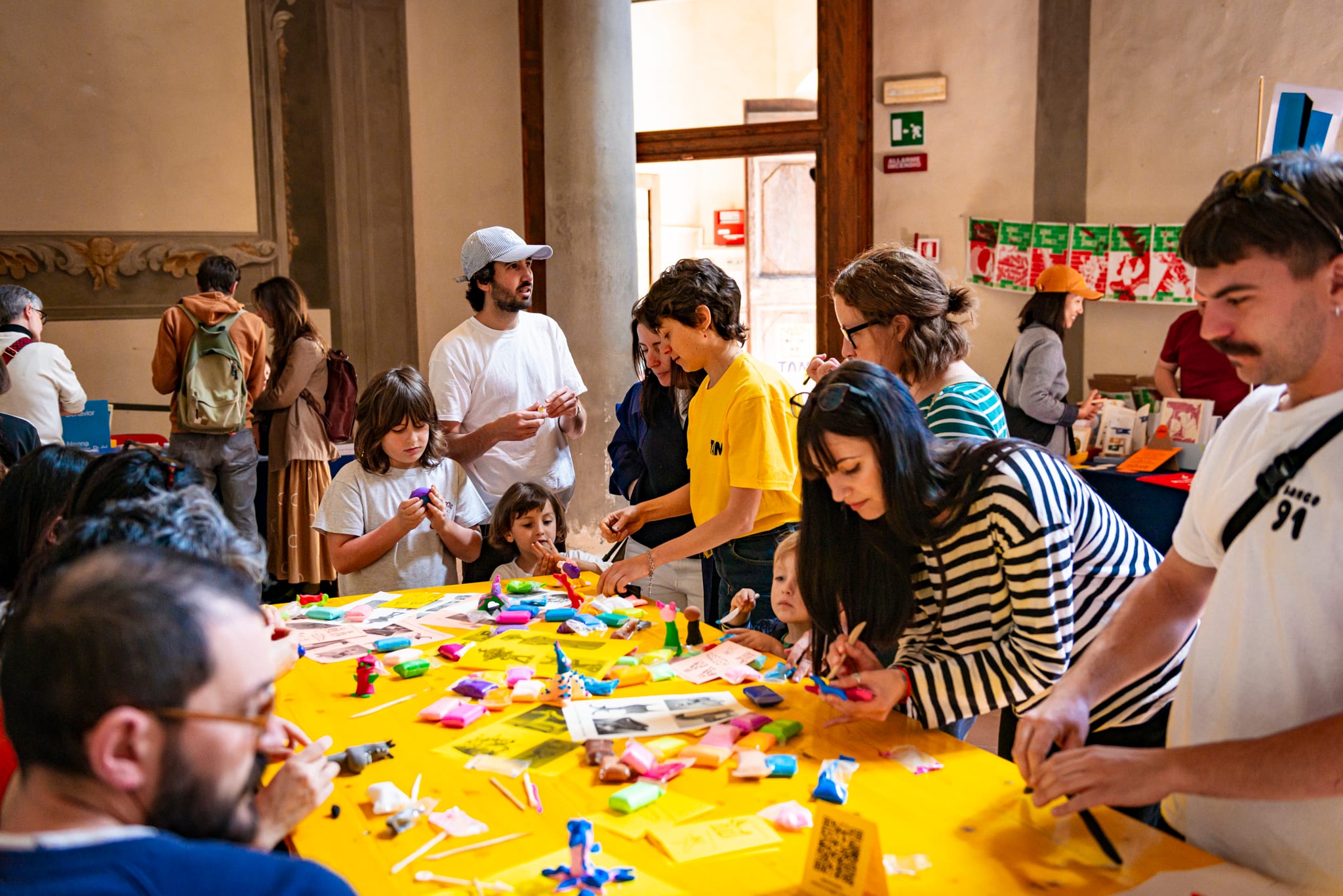 Adulti e bambini modellano la plastilina colorata attorno a un grande tavolo giallo