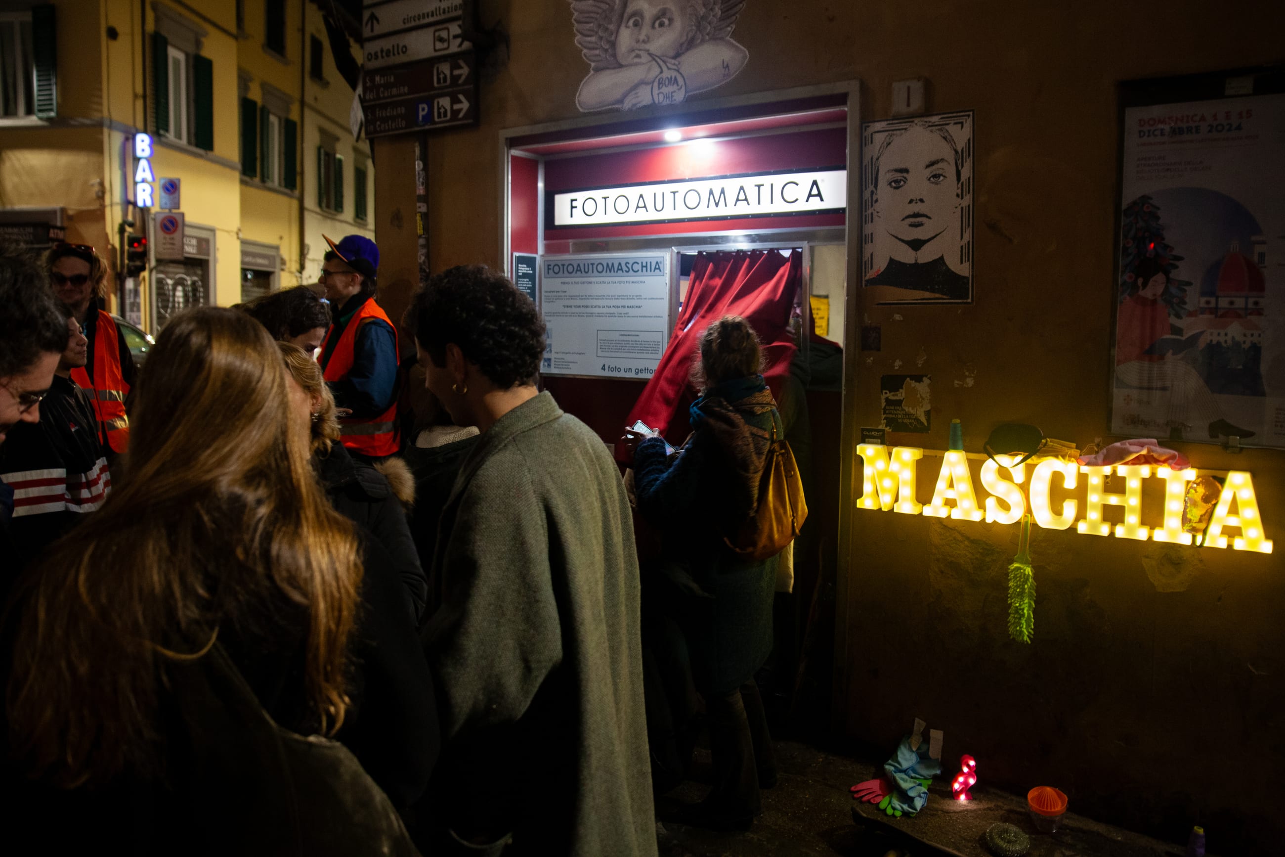 Persone di sera davanti a una cabina per fototessere con una scritta luminosa