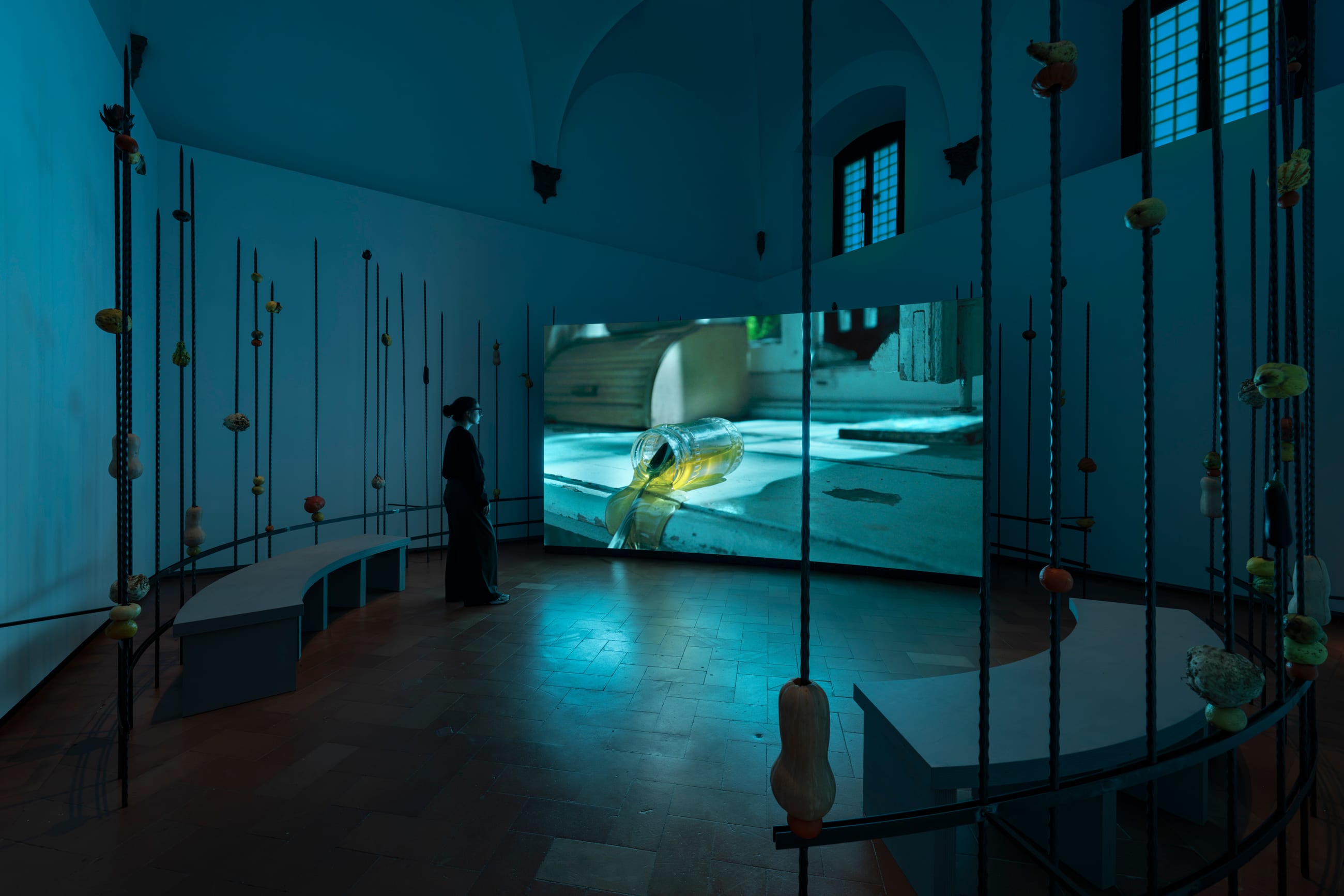 Installazione in una sala storica con aste verticali, una seduta curva e una proiezione video