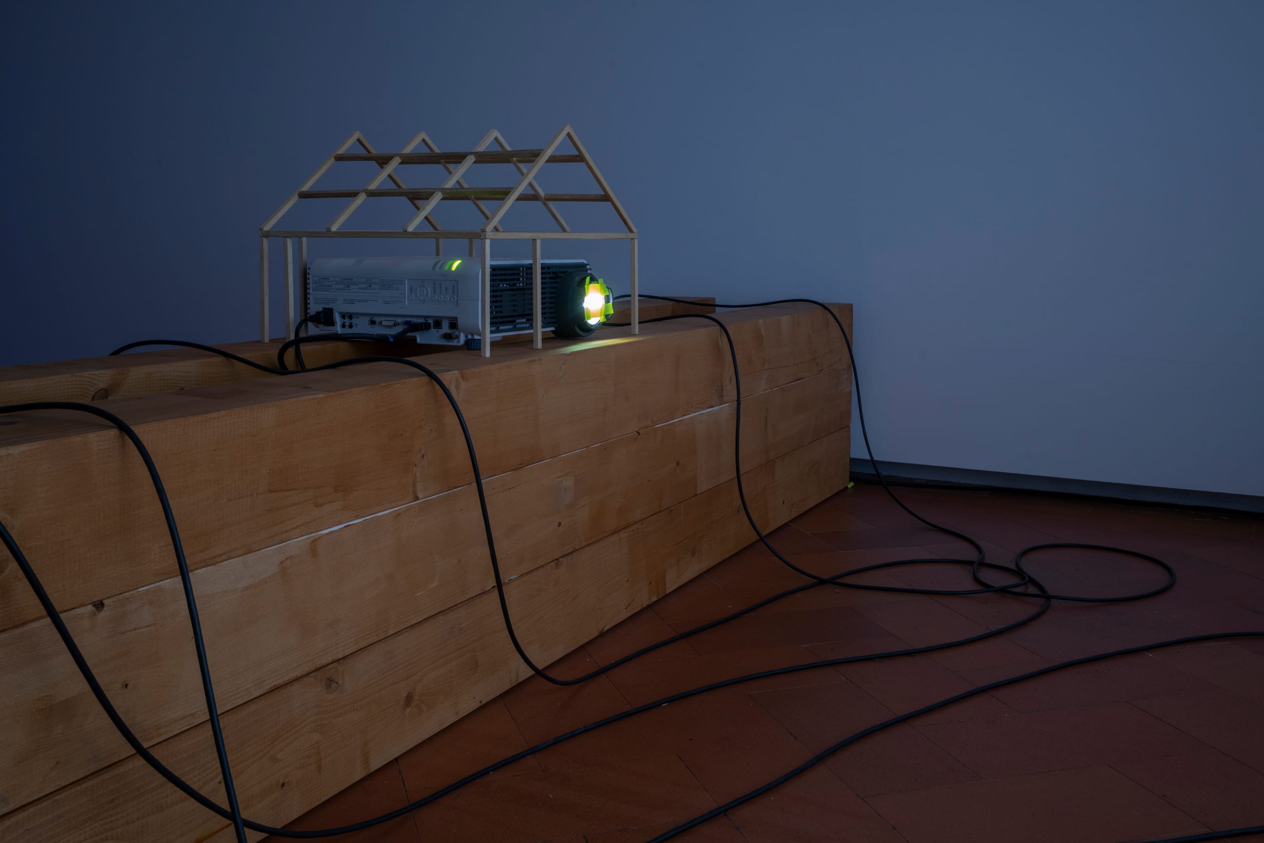 Proiettore sotto una piccola struttura a forma di casa, appoggiato su una trave in legno