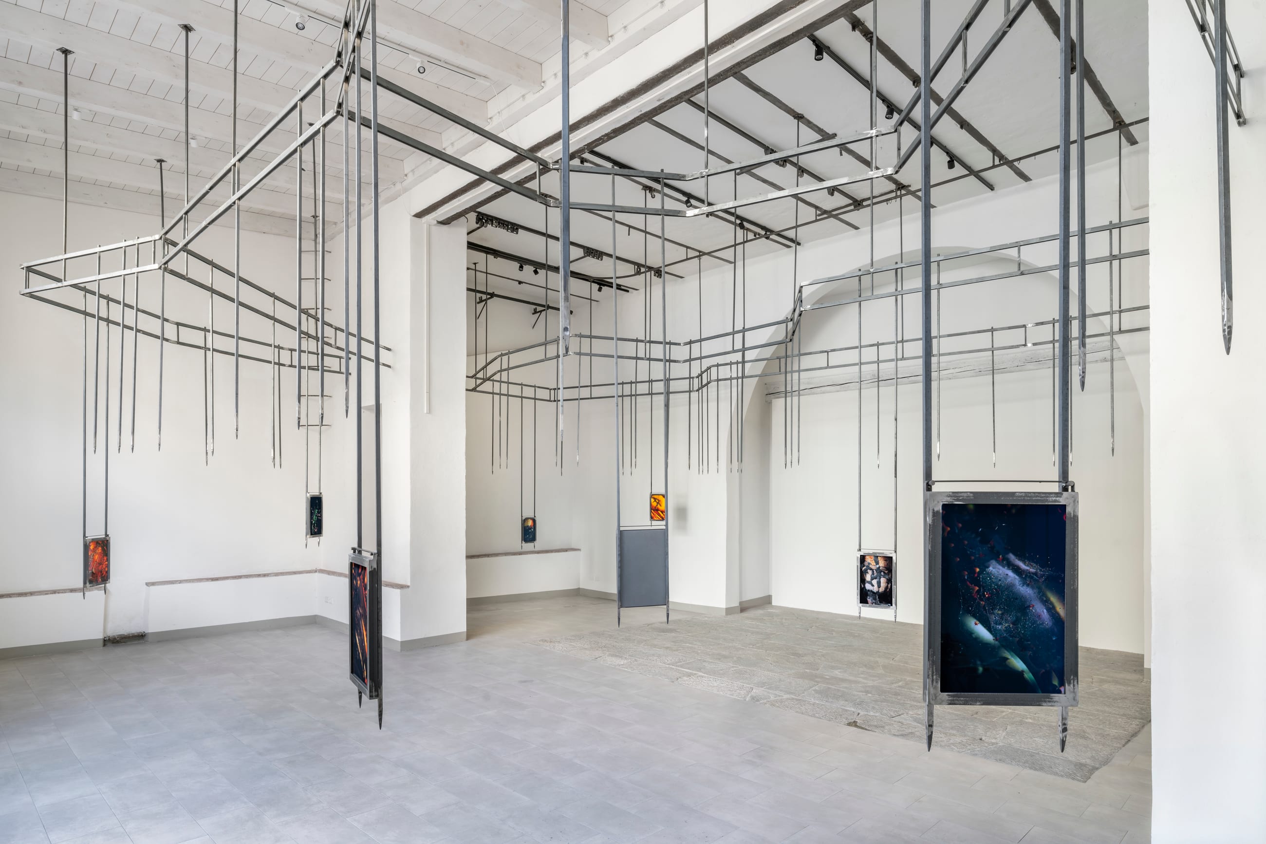 Sala bianca con una struttura metallica sospesa al soffitto da cui pendono alcune opere