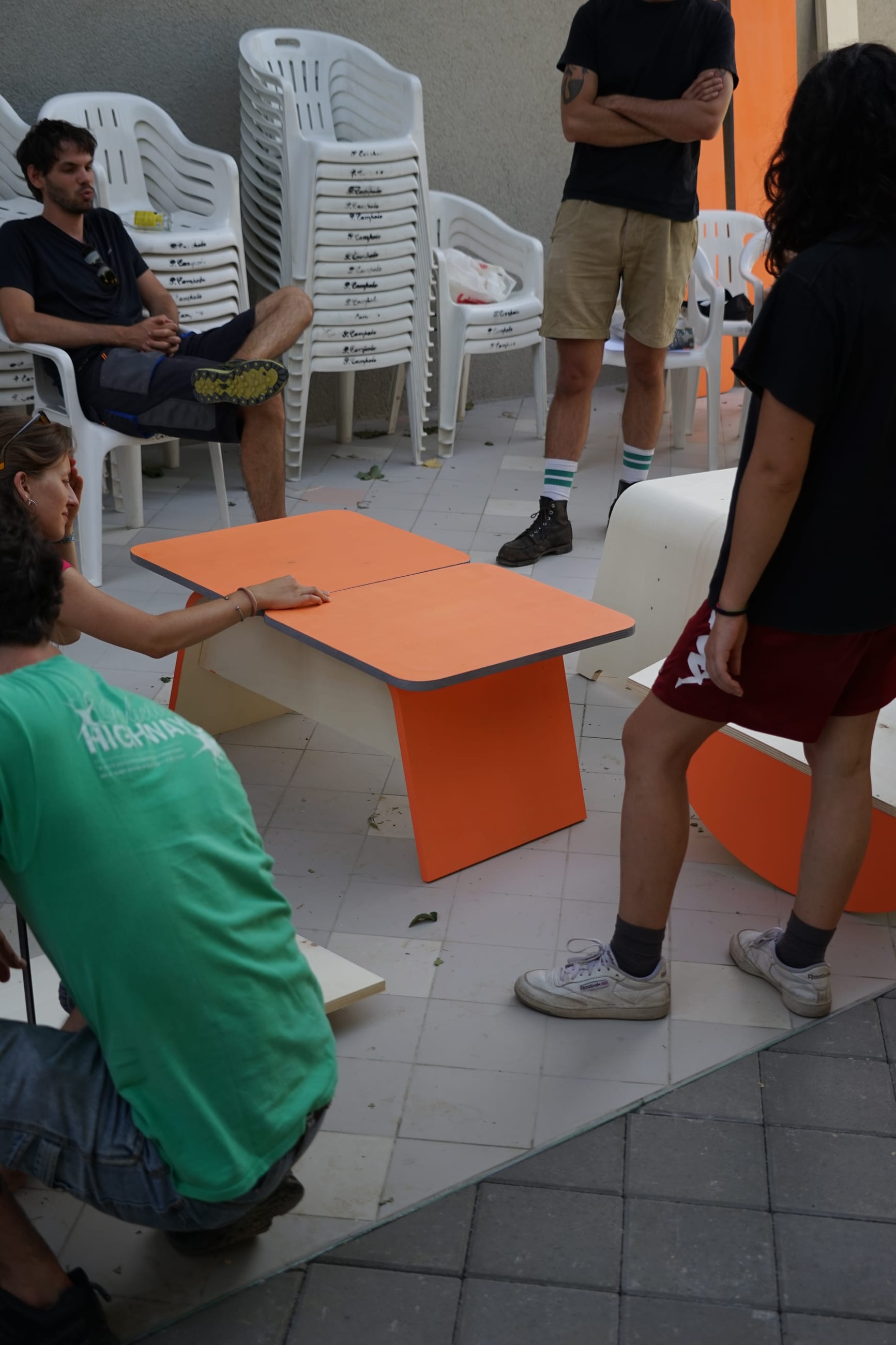 Persone attorno a un tavolino in legno arancione appena costruito, su una terrazza