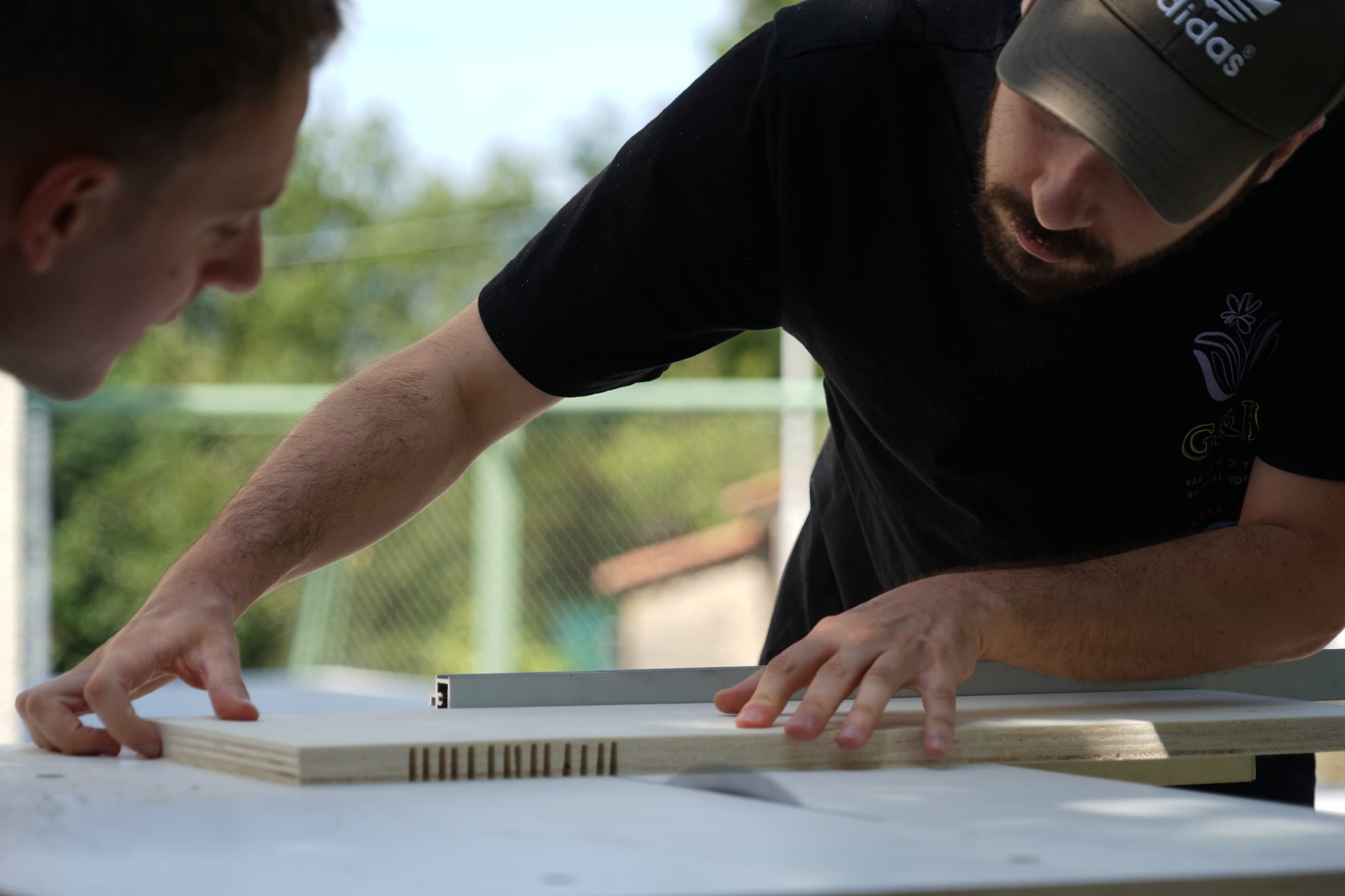 Due persone misurano un pannello in legno su un piano di lavoro all'aperto