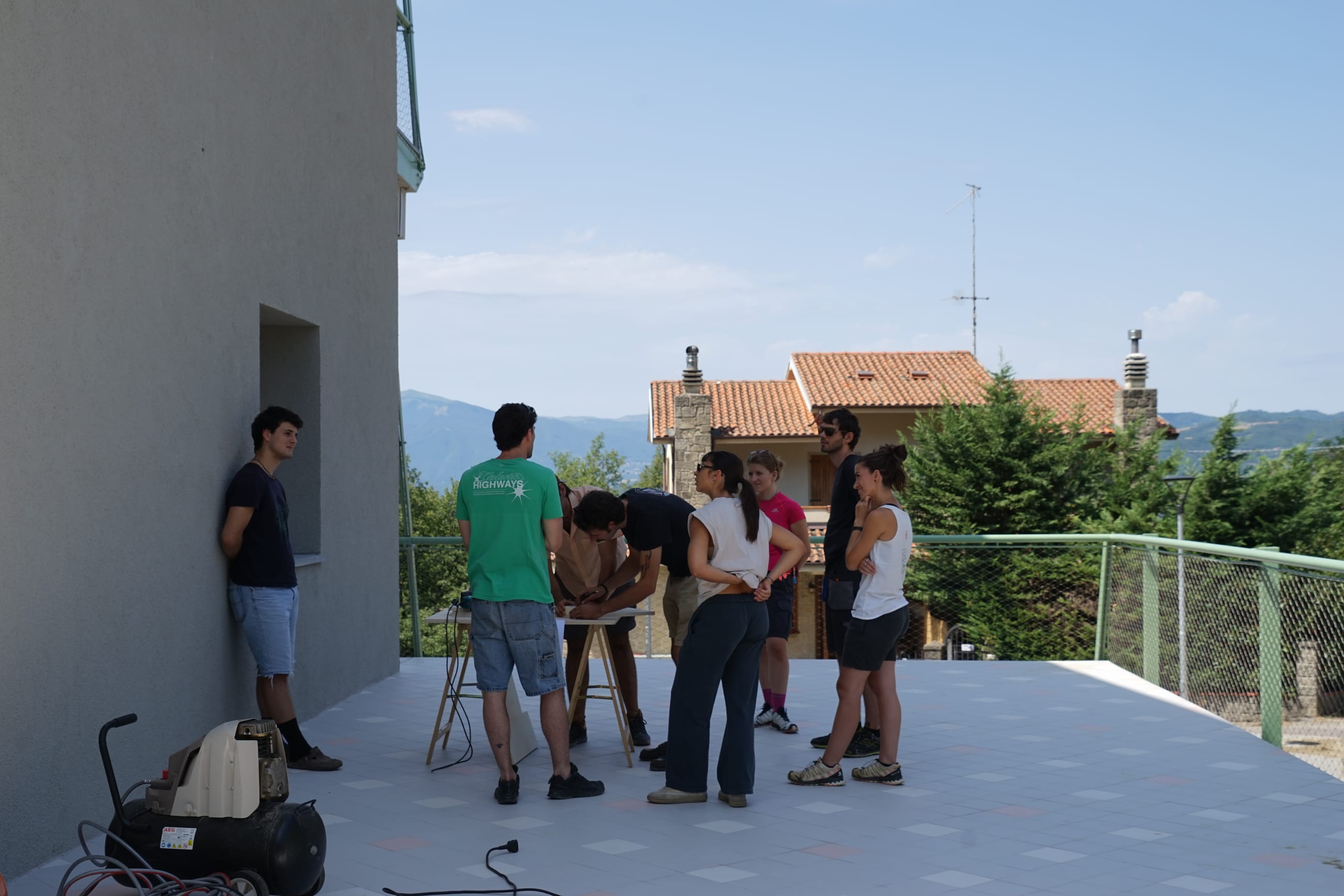 Gruppo al lavoro attorno a un banco su una terrazza, con montagne sullo sfondo