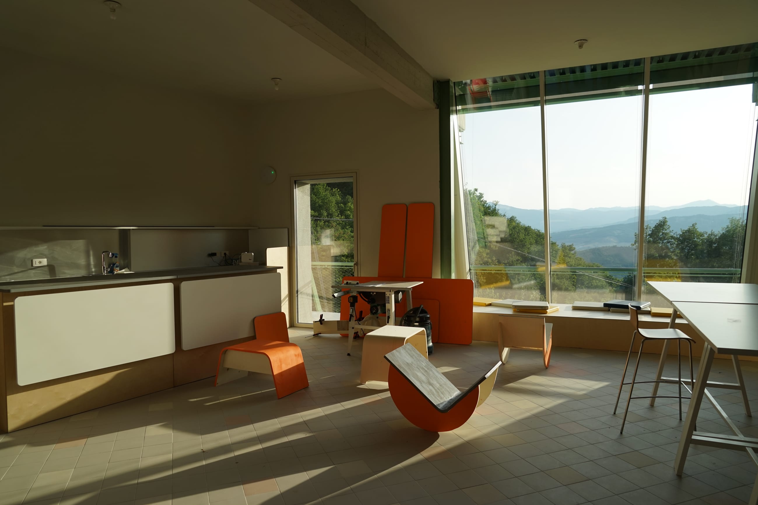 Sala luminosa arredata con sedute in legno arancione e vetrate affacciate sulle colline