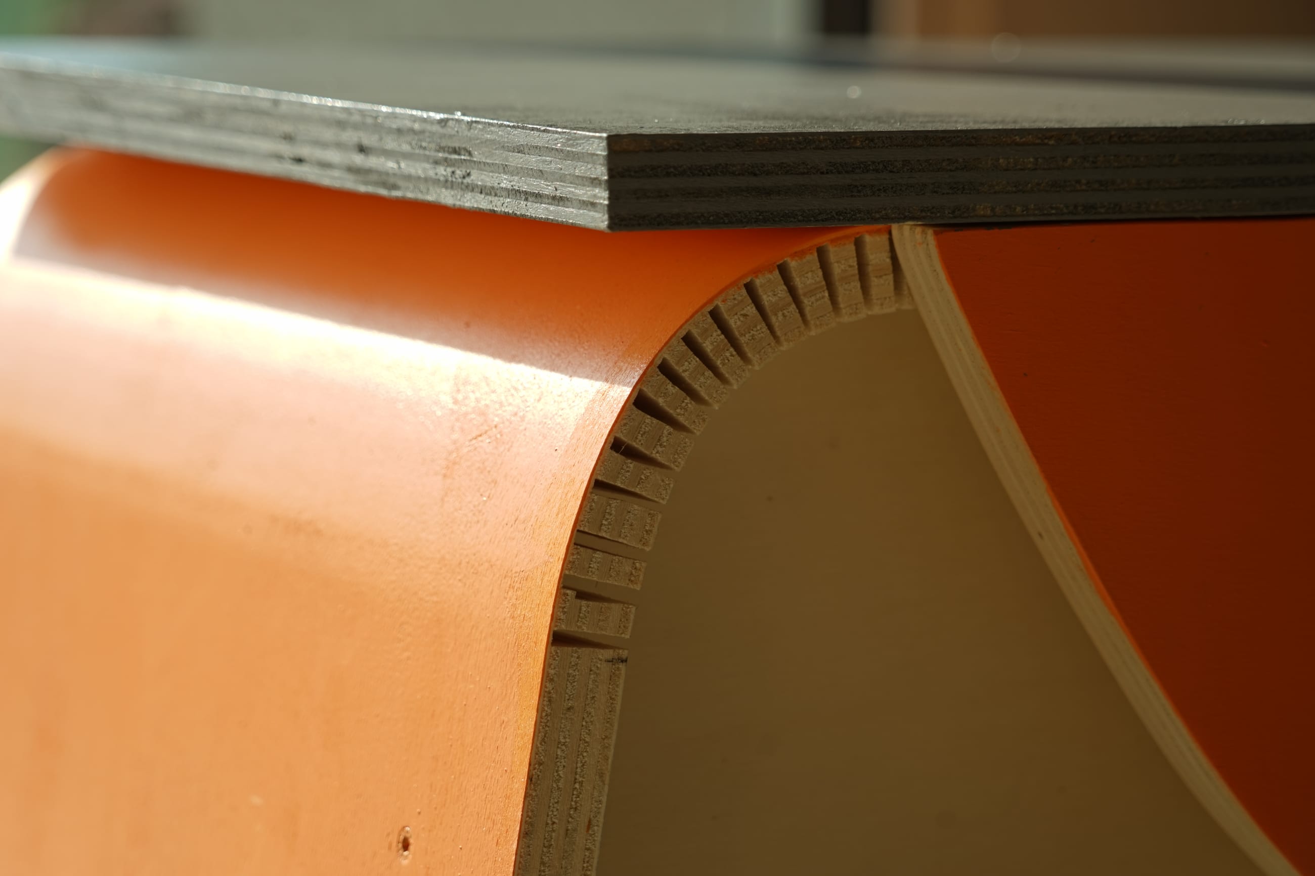 Dettaglio di un pannello in legno curvato grazie a tagli ravvicinati, con finitura arancione