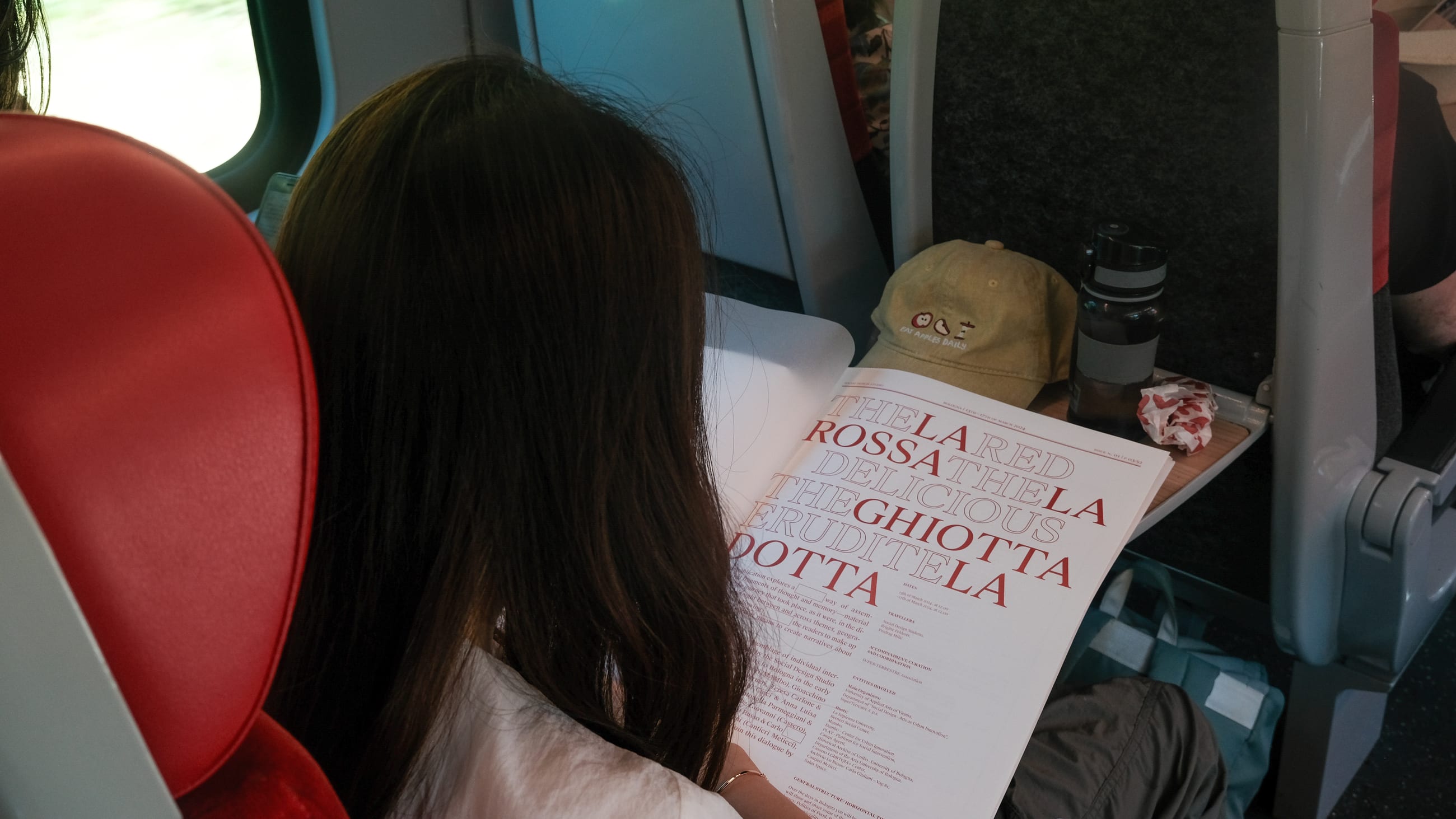 Persona in treno legge un grande foglio stampato con titoli in rosso