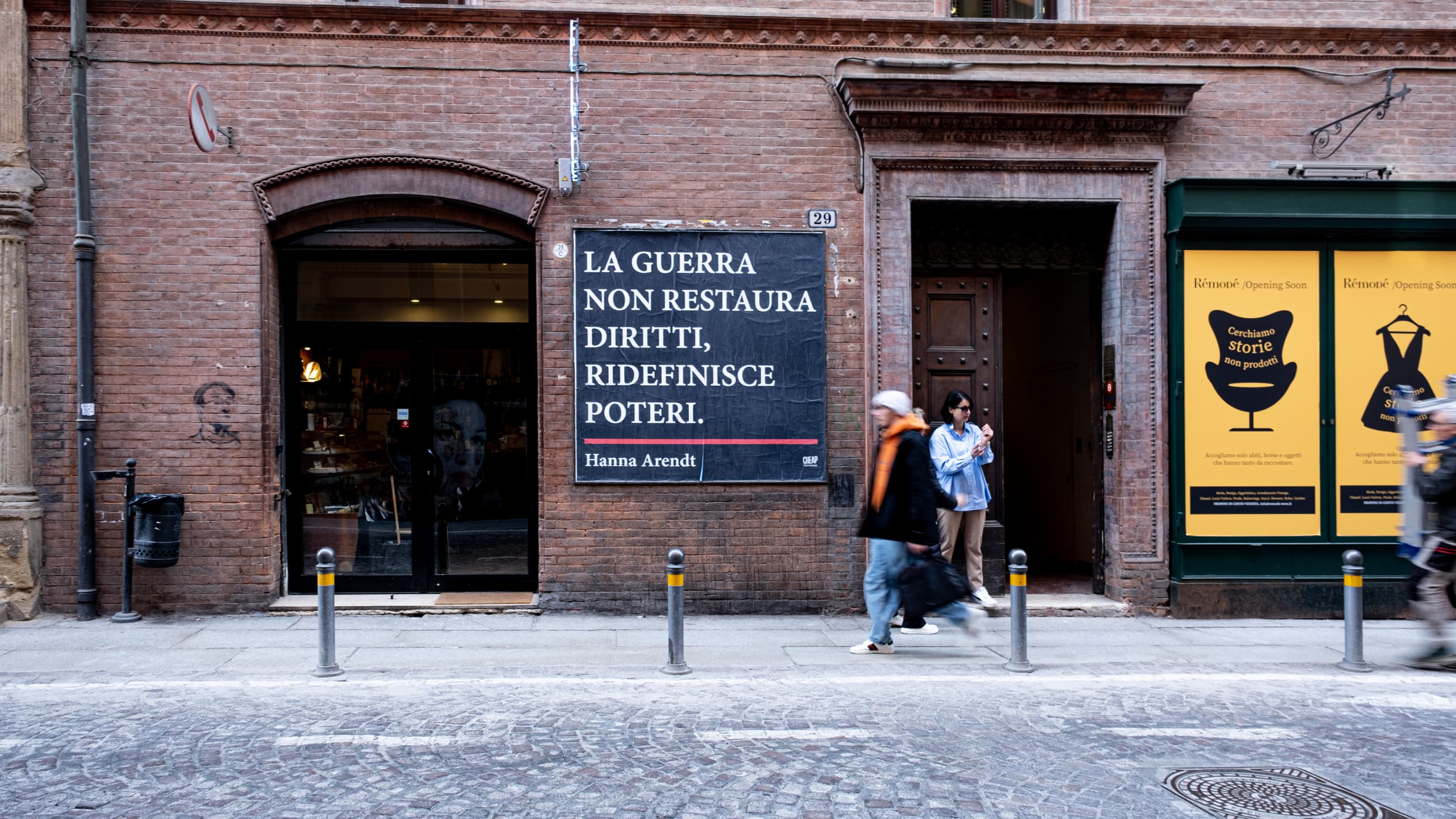 Facciata in mattoni con un manifesto nero con una citazione, mentre alcune persone passano