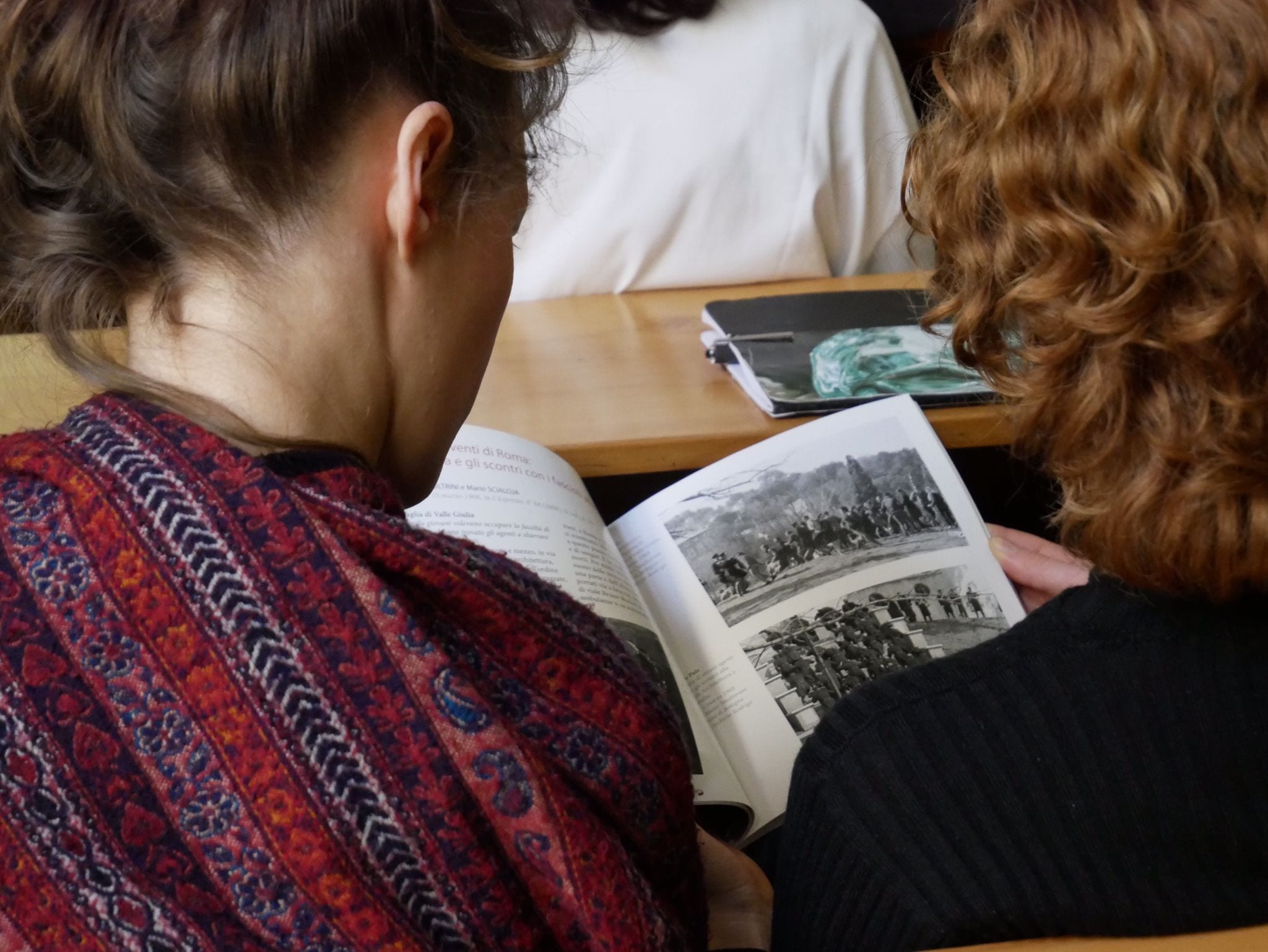 Persona sfoglia un libro con fotografie in bianco e nero, seduta in un'aula